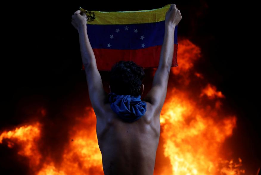 A protester holds a national flag as a bank branch, housed in the magistracy of the Supreme Court of Justice, burns during a rally against Venezuela's President Nicolas Maduro, in Caracas, Venezuela June 12, 2017. REUTERS/Carlos Garcia Rawlins TPX IMAGES 