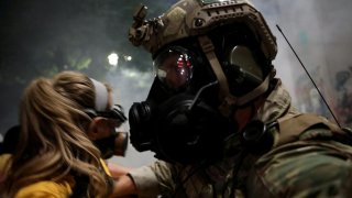 A federal law enforcement officer pushes a mother back during a demonstration against the presence of federal law enforcement officers and racial inequality in Portland, Oregon, U.S., July 21, 2020. REUTERS/Caitlin Ochs