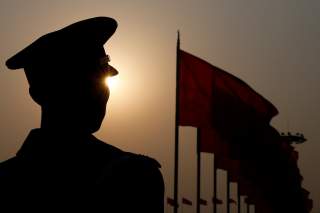 A paramilitary police officer is seen silhouetted in front of flags as he stands guard during the third plenary session of the Chinese People's Political Consultative Conference (CPPCC) in Beijing, China March 10, 2018.