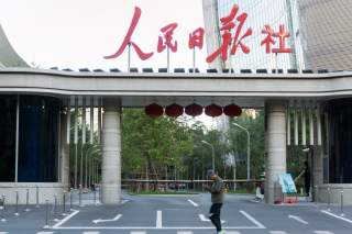 A man holding a smartphone walks past the headquarters of Chinese state newspaper People's Daily in Beijing, China October 6, 2018. Picture taken October 6, 2018. REUTERS/Stringer