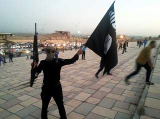 A fighter of the Islamic State of Iraq and the Levant (ISIL) holds an ISIL flag and a weapon on a street in the city of Mosul June 23, 2014. To match Exclusive MIDEAST-CRISIS/IRAQ-MOSUL REUTERS/Stringer/File Photo