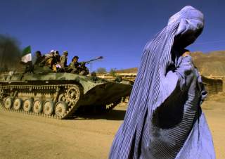 FILE PHOTO: An Afghan woman wearing a traditional Burqa walks on the side of a road as a Northern Alliance APC, (Armoured Personnel Carrier) carrying fighters and the Afghan flag, drives to a new position in the outskirts of Jabal us Seraj, some 60kms nor