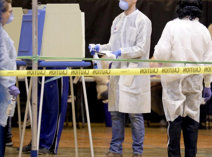 A poll worker wearing a mask to help slow the spread of coronavirus disease (COVID-19) sprays down a voting booth after use during the presidential primary election at Riverside High School in Milwaukee, Wisconsin, U.S. April 7, 2020. Mike De Sisti/Milwau