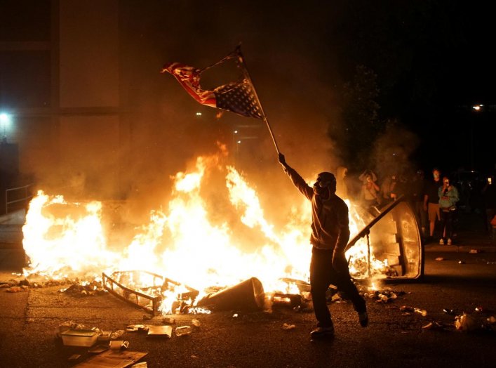 A protestor waves a burned American flag over a fire during a protest against the death in Minneapolis police custody of African-American man George Floyd, in St Louis, Missouri, U.S., June 1, 2020. Picture taken June 1,2020 REUTERS/Lawrence Bryant