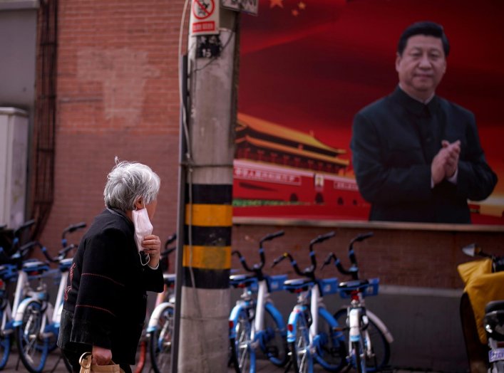 A woman with a protective mask is seen past a portrait of Chinese President Xi Jinping on a street as the country is hit by an outbreak of the coronavirus, in Shanghai, China March 12, 2020. REUTERS/Aly Song