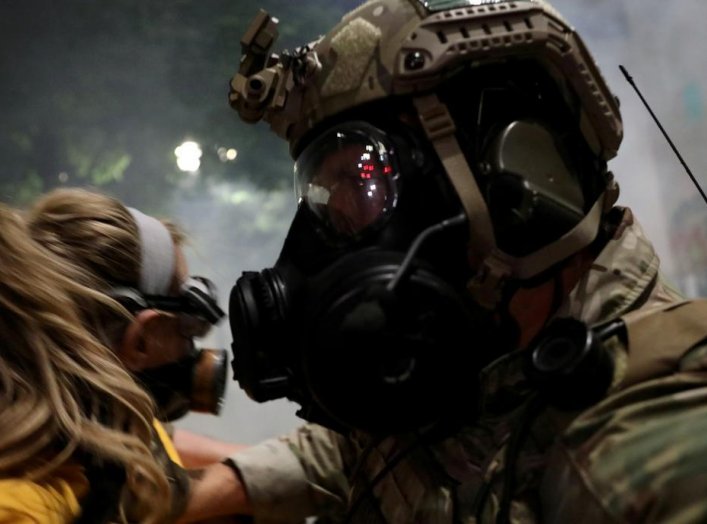 A federal law enforcement officer pushes a mother back during a demonstration against the presence of federal law enforcement officers and racial inequality in Portland, Oregon, U.S., July 21, 2020. REUTERS/Caitlin Ochs