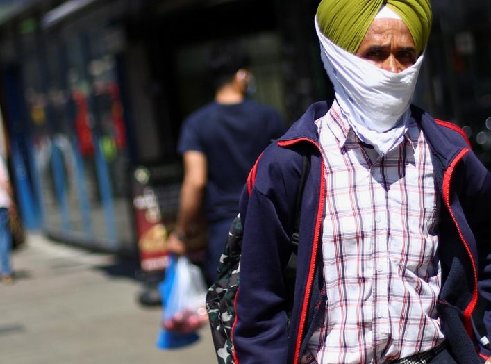 A man wears a piece of cloth as a protective mask as he walks down a street following the coronavirus disease (COVID-19) outbreak, in Ilford, London, Britain July 29, 2020. REUTERS/Hannah McKay