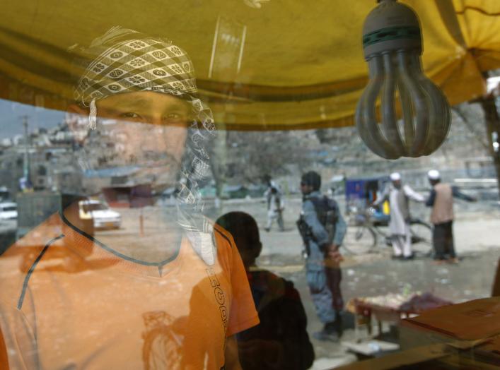 A shopkeeper stands inside a shop as people are reflected on a window panel in Kabul April 8, 2012. REUTERS/Omar Sobhani