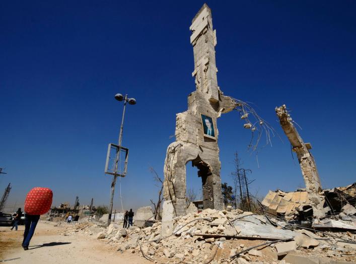 A picture of Syria's President Bashar al-Assad is displayed on a damaged structure at the entrance of al-Dukhaneya neighbourhood near Damascus, as civilians carry their belongings recovered from their homes after soldiers loyal to Syria's President Bashar