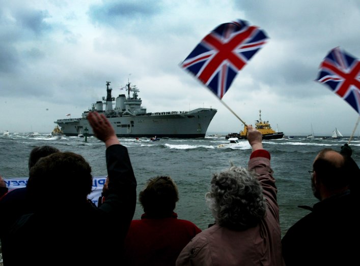 People wave as the flagship of Britain's Royal Navy HMS (Her Majesty's Ship) Ark Royal approaches Portsmouth Harbour on the coast of southern England, after operations in the Gulf conflict, May 17, 2003. REUTERS/Michael Crabtree