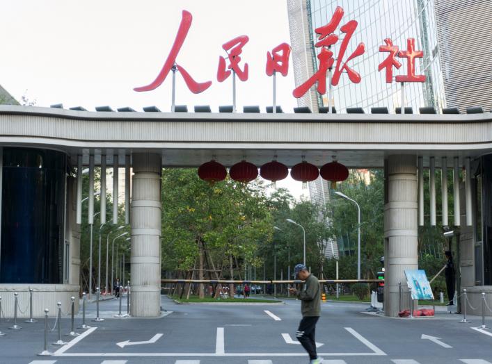 A man holding a smartphone walks past the headquarters of Chinese state newspaper People's Daily in Beijing, China October 6, 2018. Picture taken October 6, 2018. REUTERS/Stringer