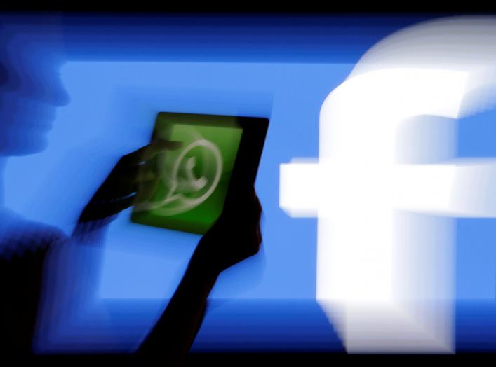 A woman holds a tablet displaying WhatsApp's logo in front of the screen with the Facebook logo in this photo illustration taken in Prague February 20, 2014. REUTERS/David W Cerny