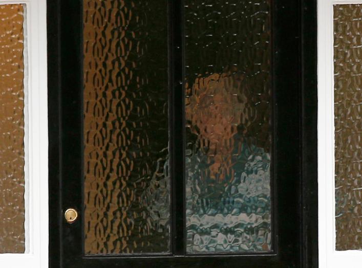 A person stands behind textured glass at an address which has been linked by local media to former British intelligence officer Christopher Steele, who has been named as the author of an intelligence dossier on President-elect Donald Trump.