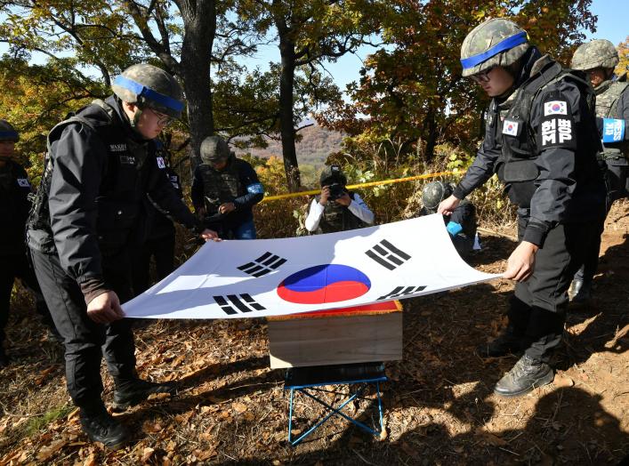 Members of South Korea's Defence Ministry recovery team cover a casket containing a piece of bone believed to be the remains of an unidentified South Korean soldier killed in the Korean War with the national flag in the Demilitarized Zone (DMZ) dividing t