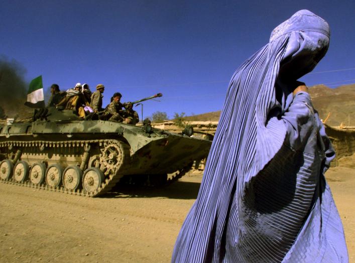 FILE PHOTO: An Afghan woman wearing a traditional Burqa walks on the side of a road as a Northern Alliance APC, (Armoured Personnel Carrier) carrying fighters and the Afghan flag, drives to a new position in the outskirts of Jabal us Seraj, some 60kms nor