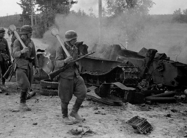 Finnish soldiers carrying Panzerfäuste on their shoulders pass by the remains of a destroyed Soviet T-34 tank at the Battle of Tali-Ihantala