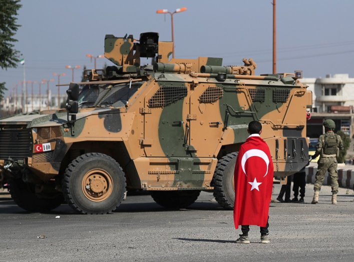 Boy wearing a Turkish flag stands in front of a Turkish military vehicle in the town of Tal Abyad